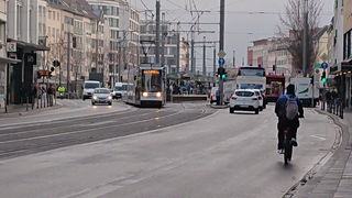 Das Verkehrsaufkommen am Bertha-von-Suttner-Platz mit Fahrrädern, Autos, LKW, einer Bahn und Fußgängern.