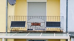 Ein Balkon an einem gelben Haus mit schwarzem Geländer, an dem zwei Photovoltaik-Module befestigt sind