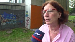 Frau mit rot-braunen Haaren steht vor Graffitiwand 