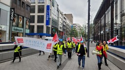 Menschen mit Bannern, Warnwesten, Fahnen und Megaphonen ziehen durch eine Fußgängerzone