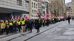 Ausgerüstet mit Fahnen, Warnwesten und Plakaten zieht eine Gruppe von Streikenden durch die Düsseldorfer Innenstadt.