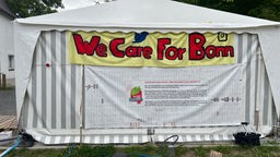 Man sieht ein Zelt mit einem Banner, auf dem in rot "We Care For Bonn" steht.