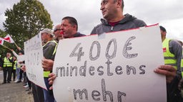 streikende Rewe Mitarbeiter die ein Plakat halten, auf dem "400€ mindestens mehr" steht