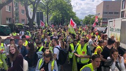 Streikende in Warnwesten und mit Verdi-Plakaten auf einer baumgesäumten Straße in Köln
