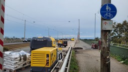 Blick auf eine Brücke, auf einer Fahrtrichtung stehen viele Baustellengeräte