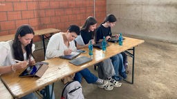 Vier junge Frauen sitzen auf einer Bank und arbeiten an Tablets.