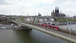 Der Langzug fährt auf der Deutzer Brücke in Köln über den Rhein. Im Hintergrund ist der Kölner Dom zu sehen.