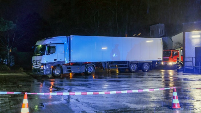 Ein LKW steht hinter Absperrband von Blaulicht beleuchtet. 