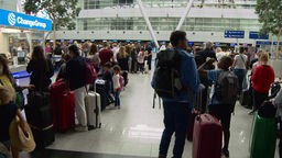 In einem Flughafen stehen viele Menschen mit Rucksäcken und Koffern.