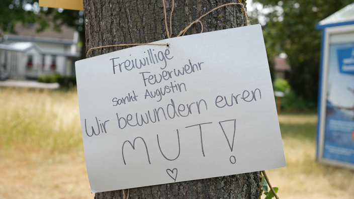 Auf einem Papierschild an einem Baum steht: "Freiwillige Feuerwehr Sankt Augustin: Wir bewundern euren Mut!"