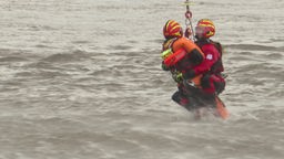 Zwei Menschen werden an einem Seil aus dem Rhein gezogen