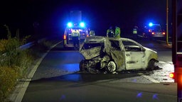 Eine Straße in der Nacht mit einem völlig zerstörten Auto, dahinter Polizisten und Blaulicht 