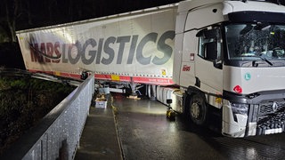 Ein LKW mit weißer Plane und der Aufschrift "MARS LOGISTICS" hängt schräg am Geländer einer Eisenbahnbrücke