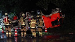 Ein Feuerwehrauto liegt auf dem Dach, davor stehen mehrere Feuerwehrleute.