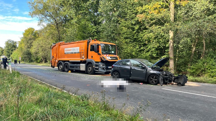 Ein Müllwagen und ein schwarzer PKW stehen sichtlich mitgenommen am Straßenrand