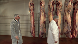 Sebastian Hielscher bei einer Begehung der Produktion einer seiner Zulieferer in einer Halle. Schweinhälften hängen von der Decke.
