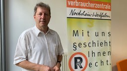 Grauhaariger Mann neben Steele und Aufschrift "Verbraucherzentrale Nordrhein-Westfalen"