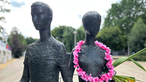 Eine Skulptur, bestehend aus einer weiblichen und einer männlichen Figur mit einem rosa Blumenkranz um den Hals der weiblichen Figur
