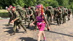 Eine Frau, von Kopf bis Fuß in pinker Kleidung, marschiert neben einer Gruppe uniformierter Soldaten
