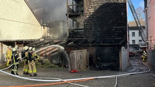 Feuerwehrleute versuchen in einem Hinterhof eine verqualmte Hausfassade zu löschen