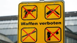 Gelbes Schild mit der Aufschrift "Waffen verboten" und durchkreuzten Waffensymbolen