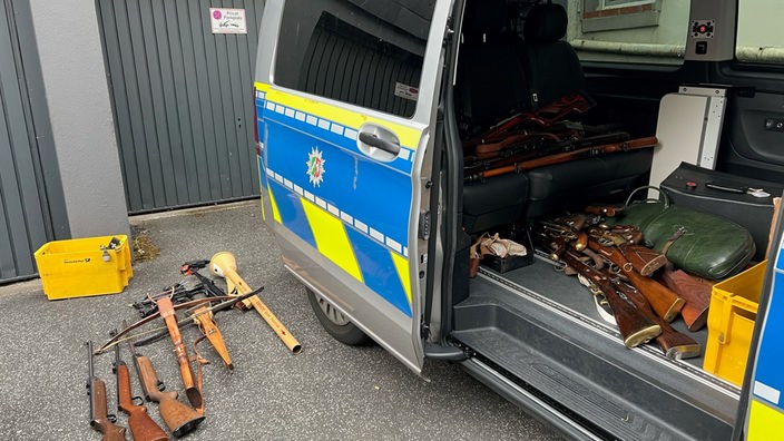 Waffen und Panzerfaust in Polizeiauto und auf dem Boden vor einer Garage