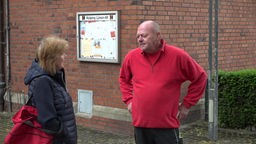 Siegfied Buchholz steht in rotem Pullover vor einer Ziegelmauer und spricht mit einem Gemeindemitglied