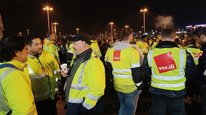 Streikende Mitarbeitende versammeln sich nachts und tragen gelbe Warnwesten.