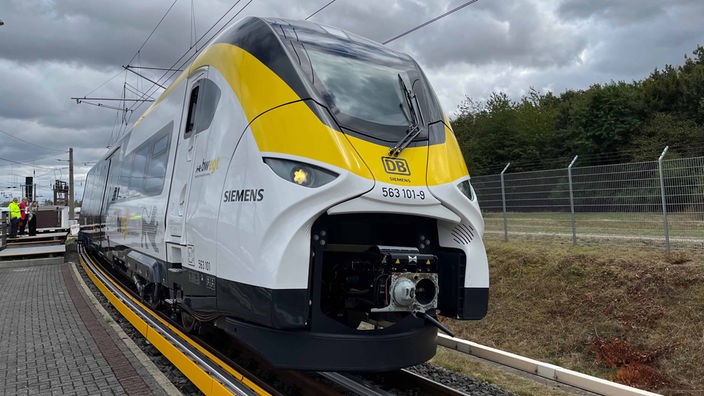 Ein weiß-gelber Zug an einem Bahnsteig unter bewölktem Himmel