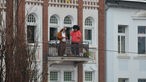 Zwei verkleidete Männer gucken dem Geschehen an Weiberfastnacht von einem Balkon aus zu.