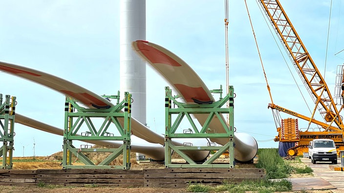 Baustelle mit Kran, im Vordergrund liegen Bauteile von Windrädern. 