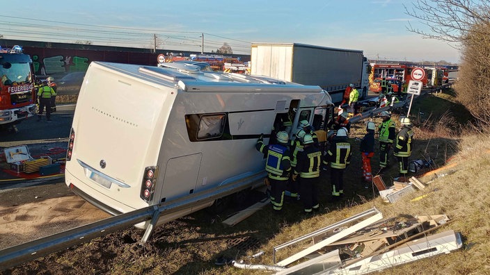 Rettungskräfte der Feuerwehr stehen am verunfallten Wohnmobil, das gegen die Autobahn-Leitplanke gelehnt ist.