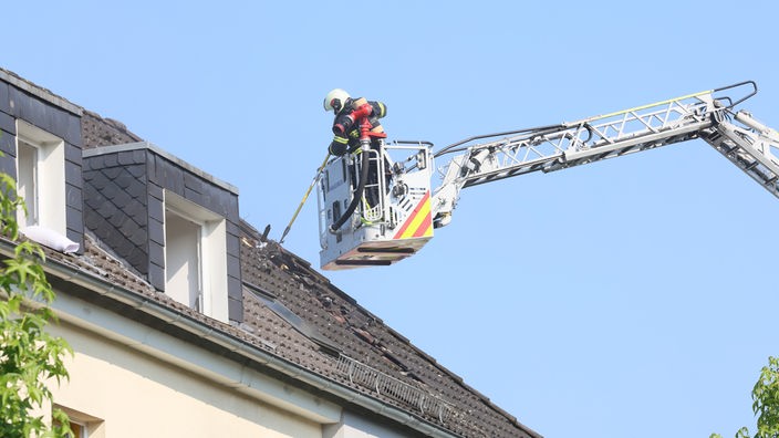 Auf dem Foto ist eine Drehleiter, in deren Rettungskorb jemand von der Feuerwehr steht und einen Dachbrand löscht.