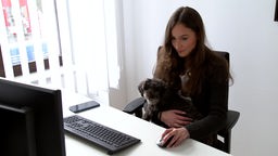Eine Frau sitzt in einem Büro, auf ihrem Schoss sitzt ein Hund.