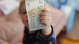 EIn Kind hält ein Fünf-Euro Schein nach oben.
