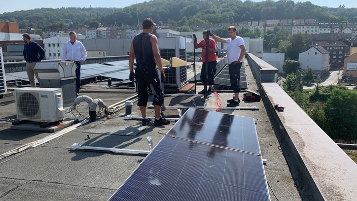 Arbeiter bauen eine Solarpanele auf einem Dach. Dahinter die Berge von Wuppertal