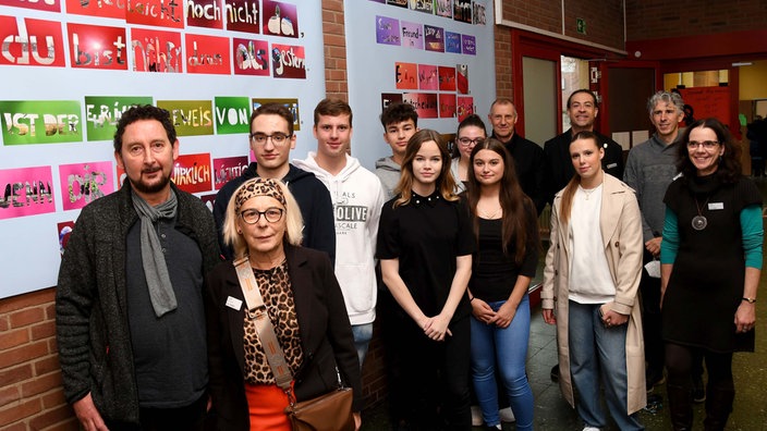 Gruppenbild mit Jugendlichen und Erwachsenen vor Wand mit bunten Karten