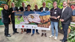 Acht Personen halten ein Banner mit einem Gecko darauf.