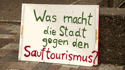 Demonstartionschild mit der Aufschrift "Was macht die Stadt gegen den Sauftourismus?"