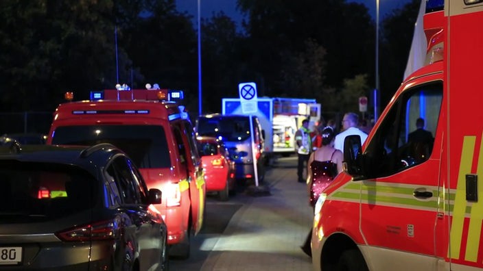 Krankenwagen und Feuerwehr autoes stehen rechts und links. In der Mitte laufen Menschen.