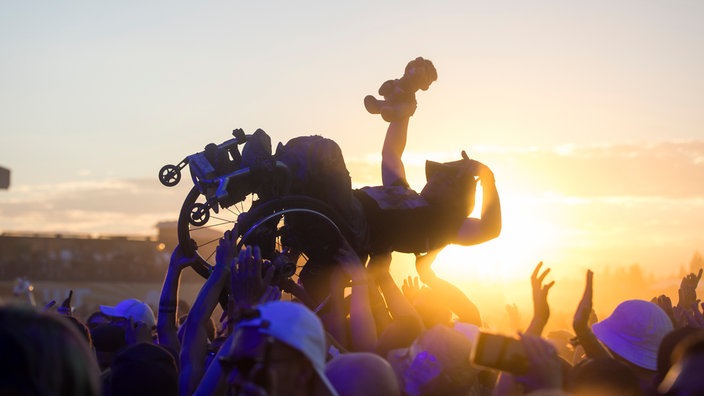 Rollstuhlfahrer wird bei einem Festival von Besuchern hochgehoben