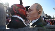 Auf einem großen Umzugswagen küssen sich eine Karnevalsfigur von Putin und eine Figur des Teufels.