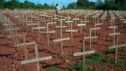 Ein Mädchen steht zwischen Gräbern in Ruanda
