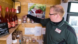 Das Bild zeigt Patrick Appelbaum, wie er ein Regal im Laden mit Marmeladengläsern bestückt.