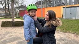 Eine Frau hilft einem Kind beim Aufsetzen des Helmes.