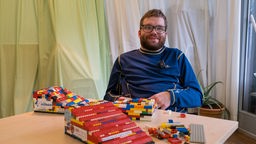 Ein junger Mann sitzt an einem Tisch und baut eine Rampe aus Lego