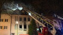 Zu sehen ist der Einsatz der Feuerwehr an einem weißen Wohnhaus mit einem Hebebühnenfahrzeug.