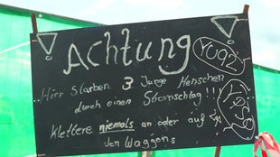 Auf einem Schild steht eine abschreckende Warnung, niemals auf den Waggons zu klettern, da daran bereits Menschen gestorben sind.