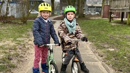 Zwei Kinder testen die neuen Helme auf ihren Laufrädern.