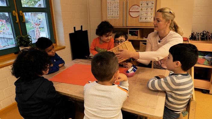 Das Bild zeigt Svitlana Bondar mit sechs Kindern bei der Arbeit. Sie hält einen Korb in der Hand und die Kinder schauen rein.